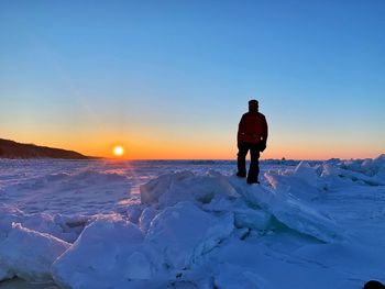 Rear view of man standing on snow against sky during sunset