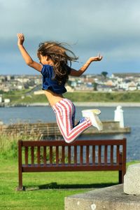 Full length of woman jumping by park bench on sunny day