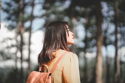 Rear view of young woman looking away against trees