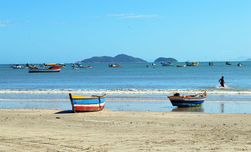 Boats moored on sea shore at beach against clear blue sky
