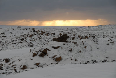 Scenic view of snow covered landscape against cloudy sky at sunset