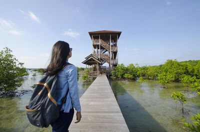 Rear view of woman standing by river against sky