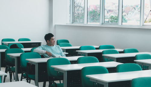 Young man looking away while sitting on table in classroom