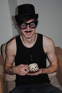 Man with coffee cup wearing funny goggles while sitting on sofa at home