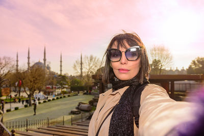 Portrait of woman standing in city against sky during sunset