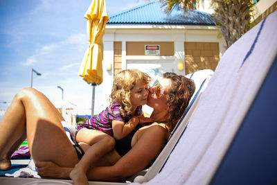 Mom and little girl on lounge chair in bathing suits giving kiss
