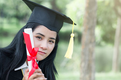 Portrait of young woman in graduation gown holding certificate