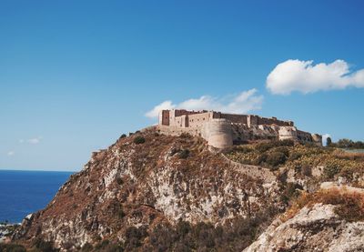 Castle by sea against blue sky in sicily