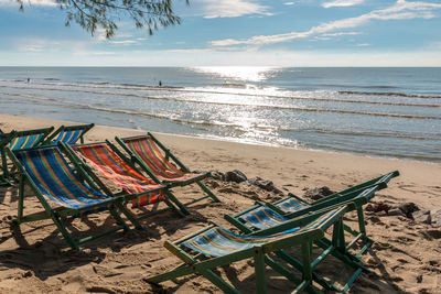 Deck chairs on beach against sky