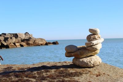 Stack of stones by sea against clear sky