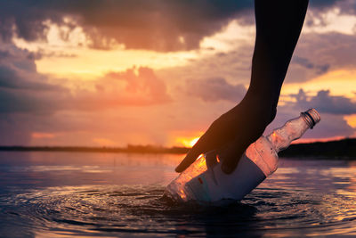 Midsection of man in sea against sky during sunset