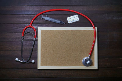 High angle view of picture frame with syringe and stethoscope on wooden table
