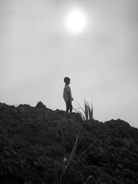 Low angle view of boy standing on rock against sky