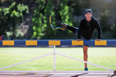 Portrait of young athlete stretching prosthetic leg on railing at running track