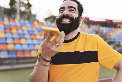 Happy bearded man talking on smart phone through speaker