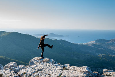 Man standing on rock at mountain peak against sky