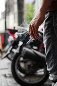 Cropped image of man holding cigarette while standing on street