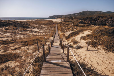 Boardwalk leading towards sea against clear sky