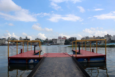Pier over river by buildings against sky