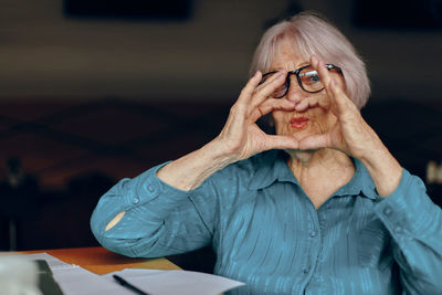 Portrait of senior woman making heart shape at cafe