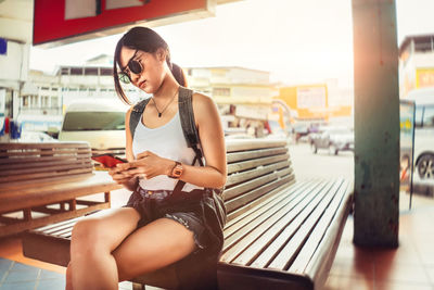 Young woman using mobile phone while sitting on laptop