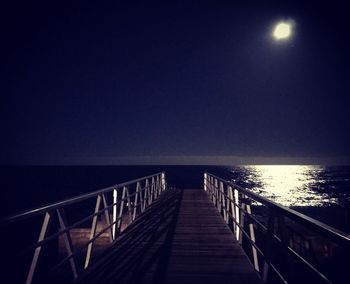 Jetty in sea against clear sky at night