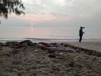 Man standing on beach against sky during sunset