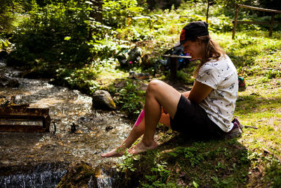 Side view of woman sitting by plants against trees