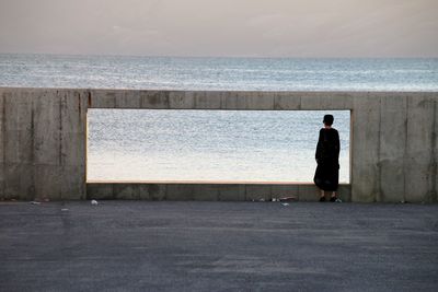 Rear view of woman standing by ocean against sky