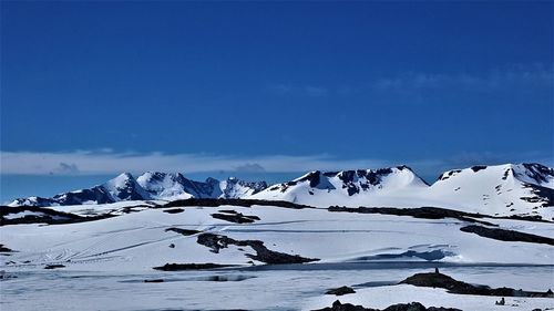 Idyllic shot of frozen river by snowcapped mountains against blue sky