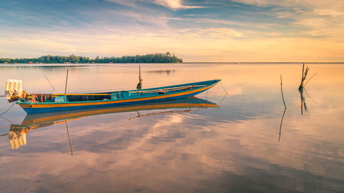 Boat moored in lake against sky during sunset