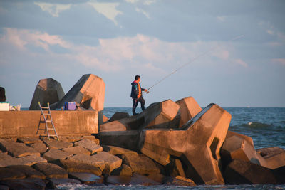 Men standing on cliff by sea against sky