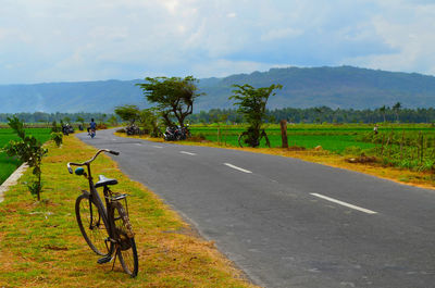 Bicycle parked by road against sky