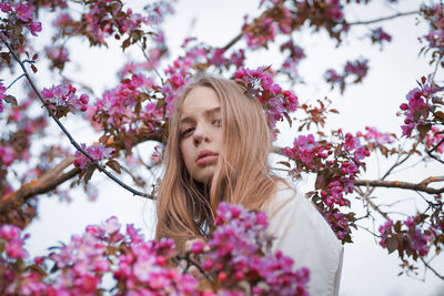 Portrait of young woman with pink cherry blossoms against trees