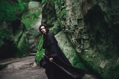 Portrait of smiling young woman standing on rock in forest