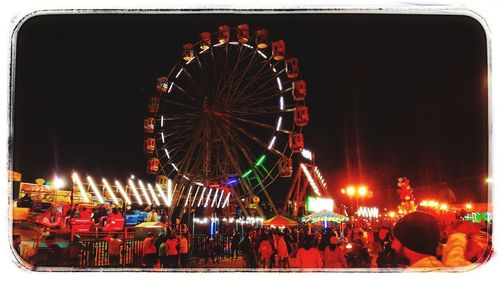 Illuminated ferris wheel in amusement park against sky at night