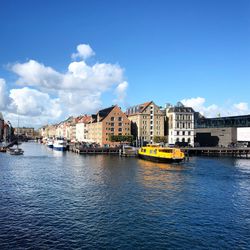 Buildings by river against blue sky