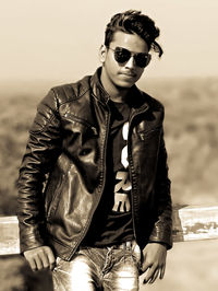 Portrait of young man wearing sunglasses and leather jack while standing outdoors