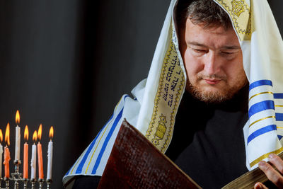 Man wearing scarf reading book by colorful burning candles