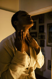 Young woman applying moisturizer on neck at home