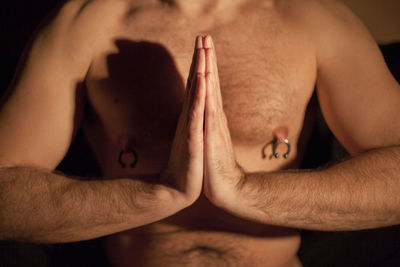 Midsection of shirtless man doing yoga at home