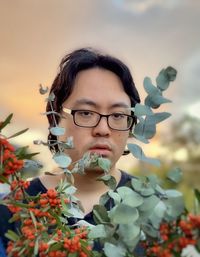 Young asian man with orange rowan berries and eucalyptus leaves against sunset sky.