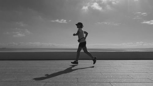 Side view full length of woman jogging at promenade against sky