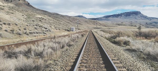 Railroad track leading towards mountain range against sky