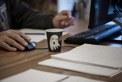 Midsection of man using computer by disposable cup on table