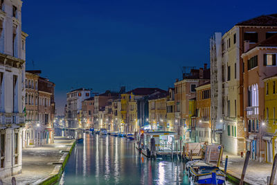 Boats in canal amidst buildings against sky at dusk