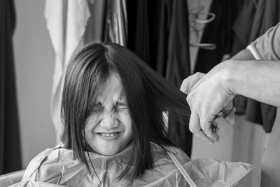Asian young girl with funny expression is getting haircut at home. monochrome, black and white.