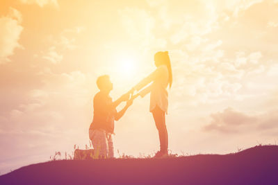 Side view of couple standing against sky during sunset