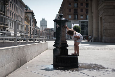 4 year-old girl drinks water from a public water fountain in milan, next to close to porta nuova.