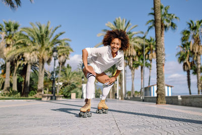 Portrait of mid adult woman roller skating against blue sky